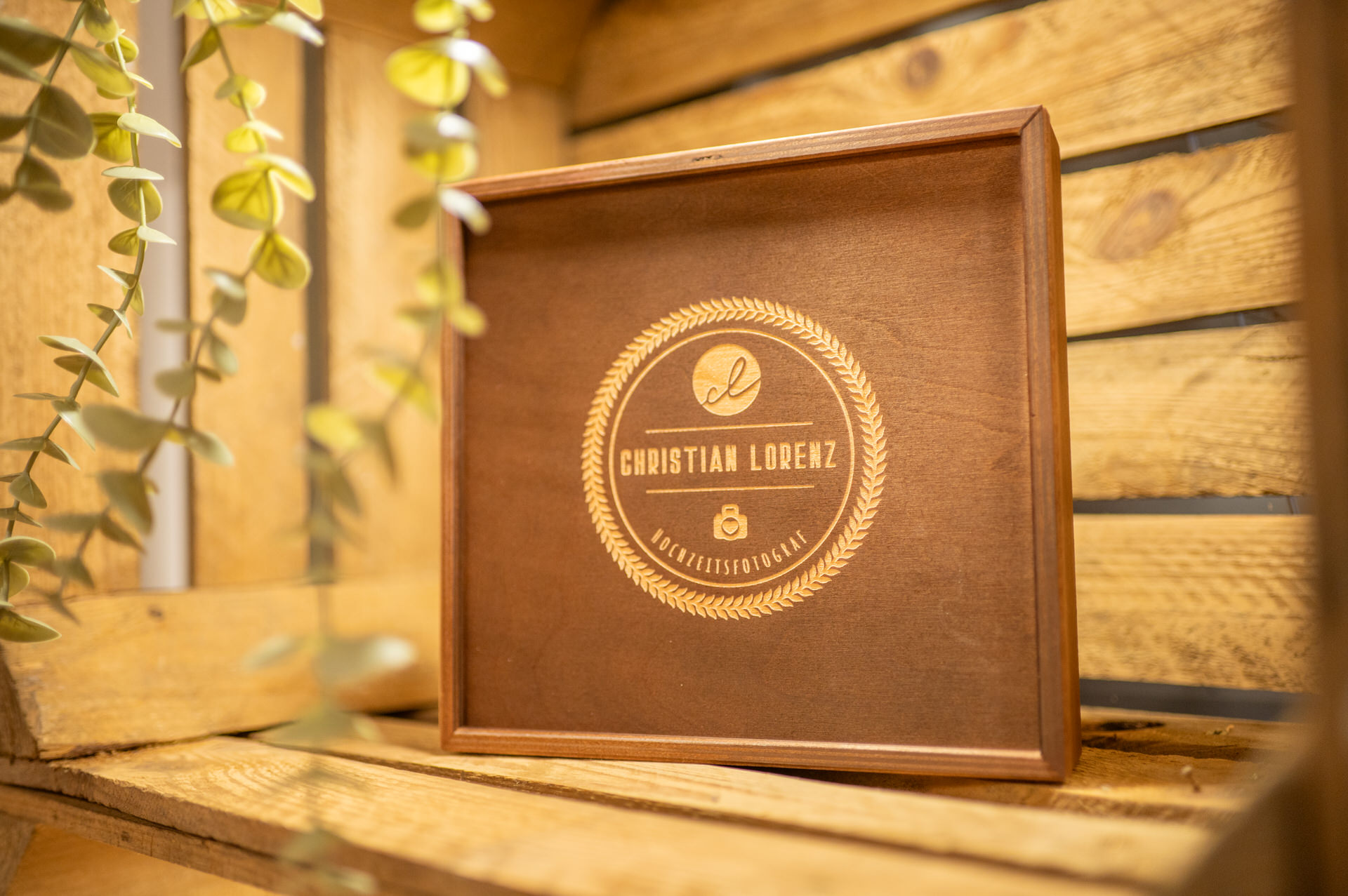 Holztafel mit der Gravur „Christian Lorenz“ und Logo auf einem mit Laubwerk verzierten Holzhintergrund.